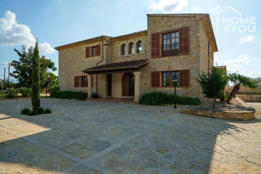 Traditionelles Steinhaus mit großem gepflasterten Vorplatz und mediterraner Bepflanzung.