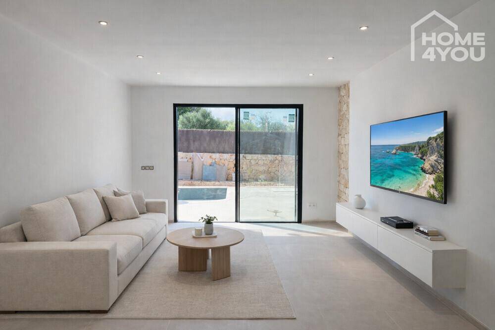 Helles Wohnzimmer mit beigem Sofa, modernem TV und Zugang zum Außenbereich.