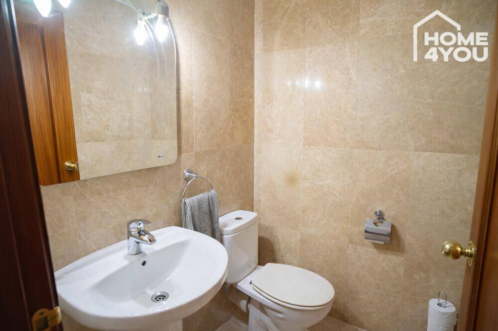 Kleines WC mit beigefarbenen Fliesen, Standwaschbecken und Toilette.
