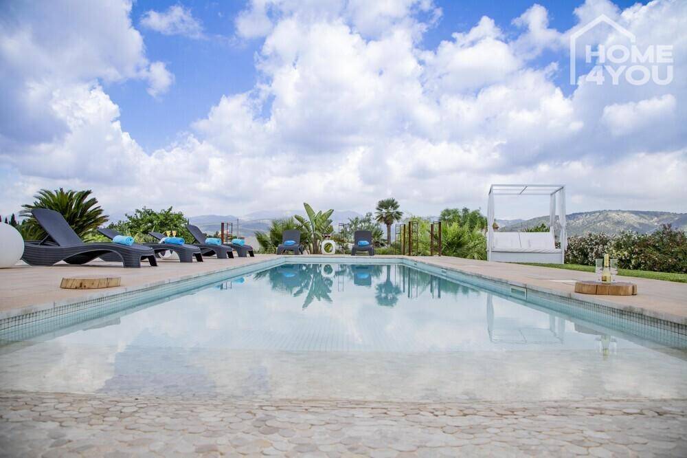 Großer Swimmingpool mit Liegestühlen und einem Himmelbett, umgeben von mediterraner Landschaft.