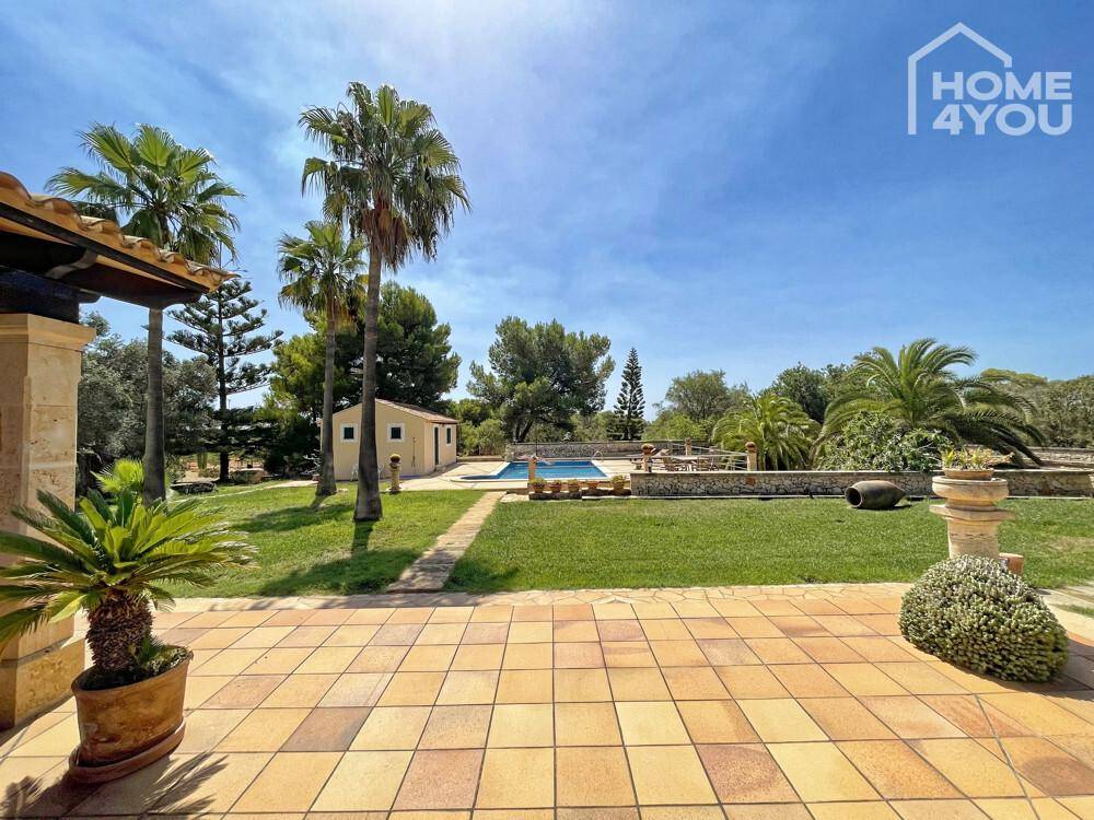 Weitläufige Terrasse mit Blick über den grünen Rasen zum Pool und einem kleinen Nebengebäude.