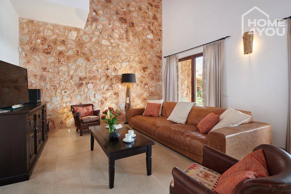 Gemütliches Wohnzimmer mit Natursteinwand, Ledersofa und dunklen Holzmöbeln.