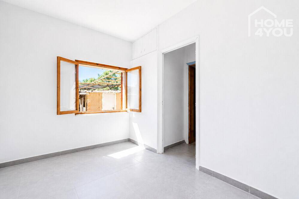 Einfaches Schlafzimmer mit Fliesenboden, weißen Wänden und einem Fenster, das viel Licht hereinlässt.