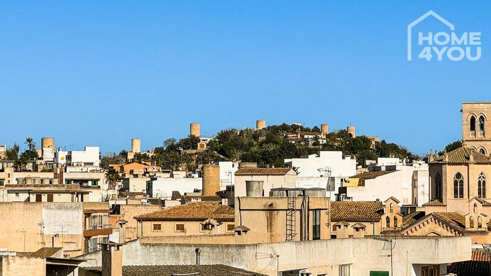 Panoramablick über die Dächer der Stadt mit historischen Türmen und Hügeln im Hintergrund.