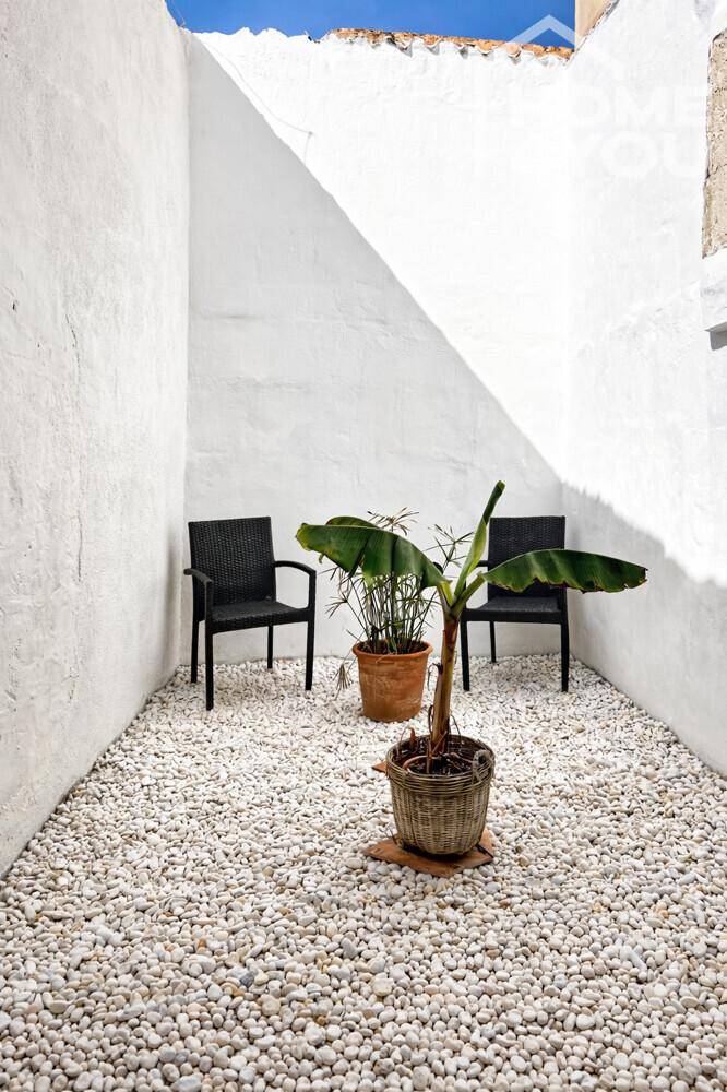 Minimalistischer Innenhof mit Kiesboden und zwei Stühlen, umgeben von hohen weißen Wänden.