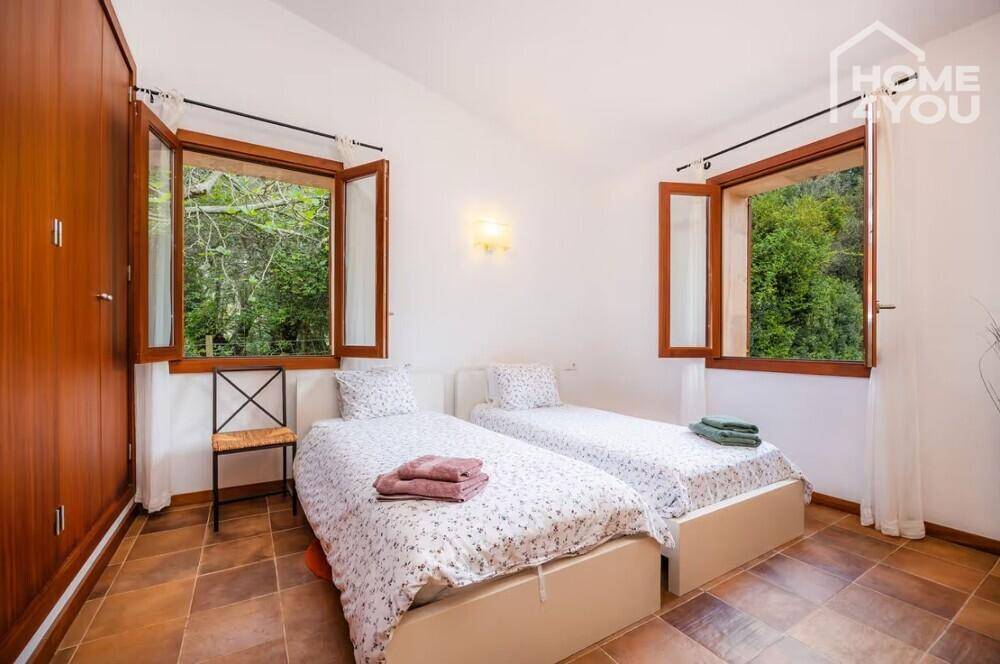 Helles Schlafzimmer mit zwei Einzelbetten, Holzboden und Fenstern mit Blick auf die Natur.