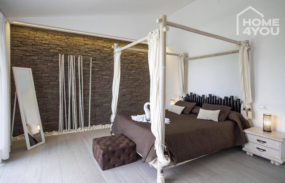 Gemütliches Schlafzimmer mit Himmelbett, Steinwandakzent und stilvoller Dekoration.