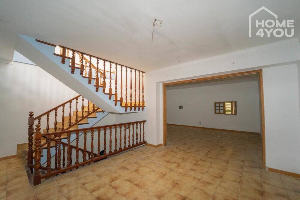 Heller Eingangsbereich mit beeindruckender Holztreppe und Fliesenboden, der zu weiteren Räumen führt.