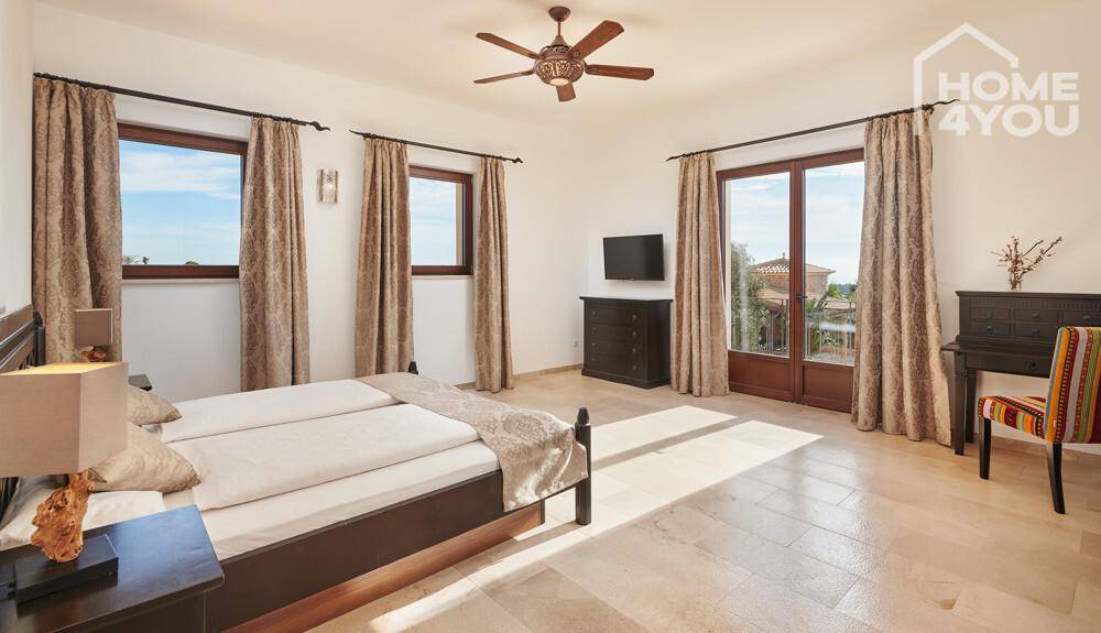 Großes Schlafzimmer mit Deckenventilator, Fliesenboden und Zugang zu einem Balkon.