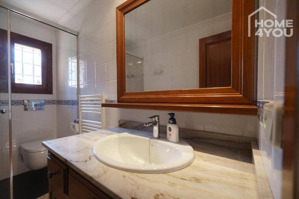 Badezimmer mit Einzelwaschbecken, großem Spiegel und hellen Fliesen.
