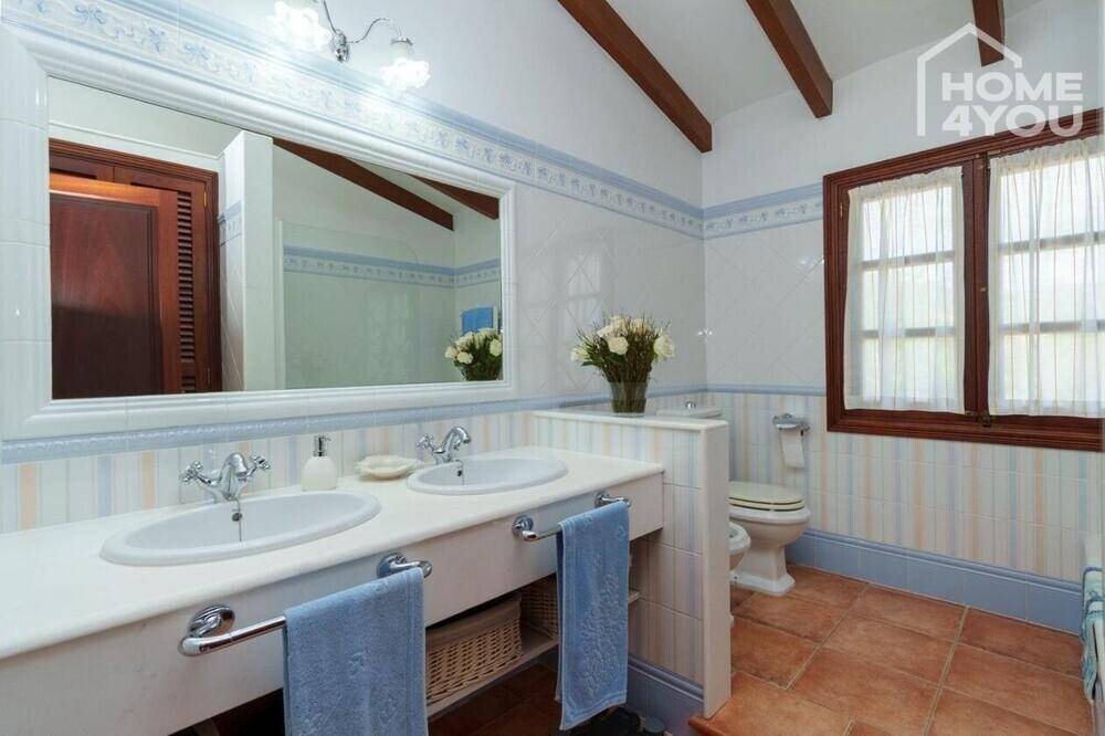 Helles Badezimmer mit Doppelwaschbecken, WC und traditionellen Fliesen in Pastellfarben.
