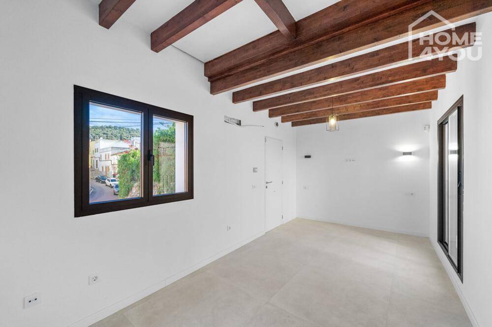Leerer, heller Raum mit weißen Wänden, Holzbalkendecke und großem Fenster zur Straße.