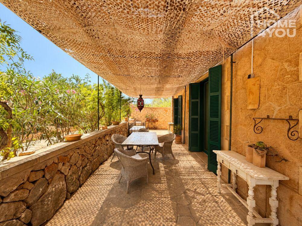 Überdachte Terrasse mit Esstisch und Stühlen, umgeben von mediterraner Vegetation.