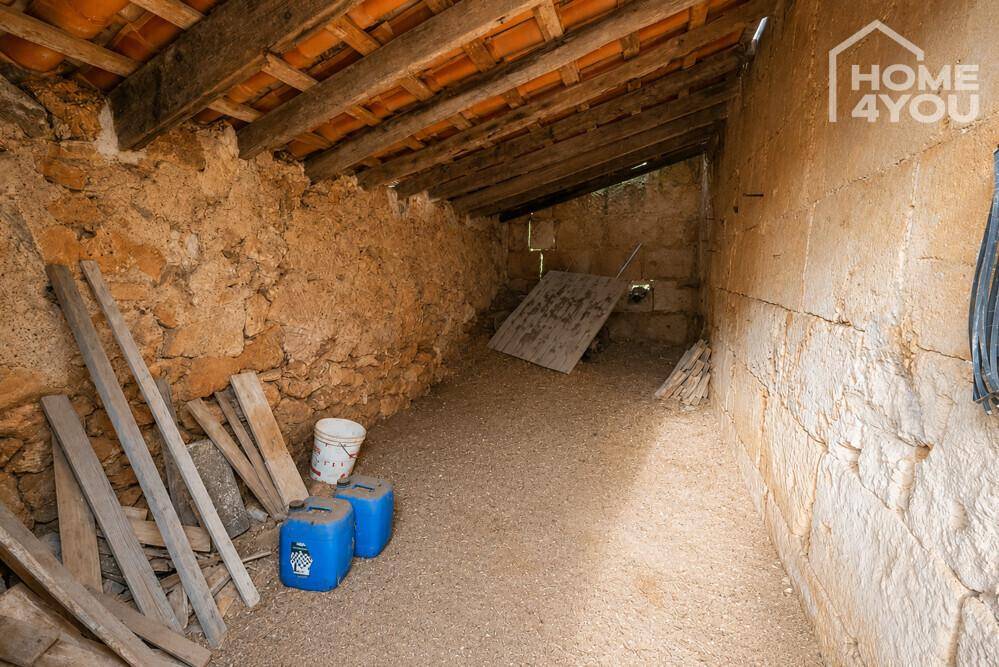 Rustikaler Innenraum mit unverputzten Steinwänden, Holzbalkendecke und losem Schotterboden.