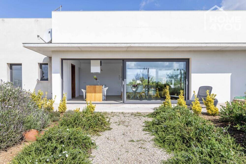 Moderne Hausfassade mit großen Glasschiebetüren und einem Kiesweg durch den Garten.
