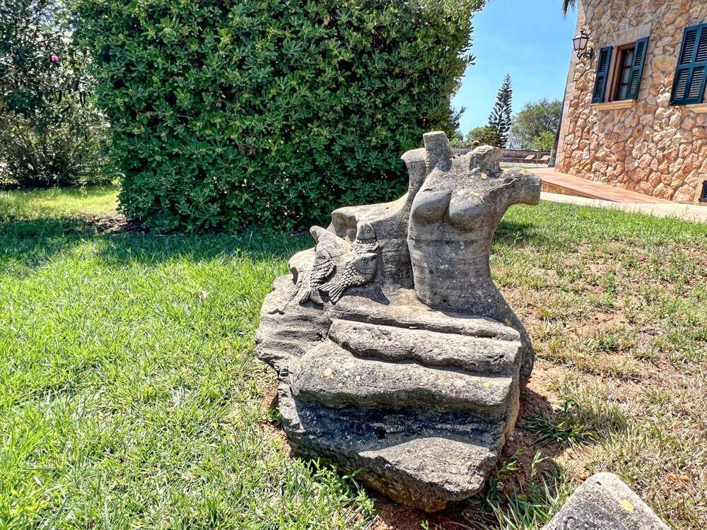 Abstrakte Steinskulptur auf einer grünen Rasenfläche, die das mediterrane Ambiente unterstreicht.