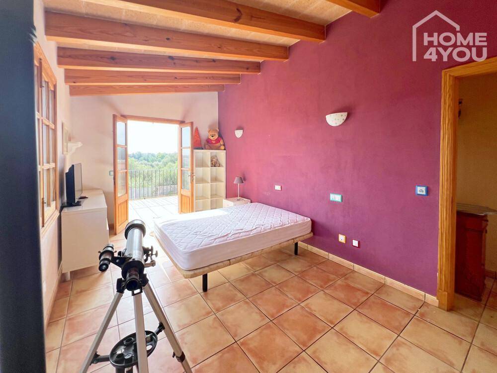 Schlafzimmer mit Holzbalkendecke, Fliesenboden und Zugang zu einem Balkon mit Weitblick.