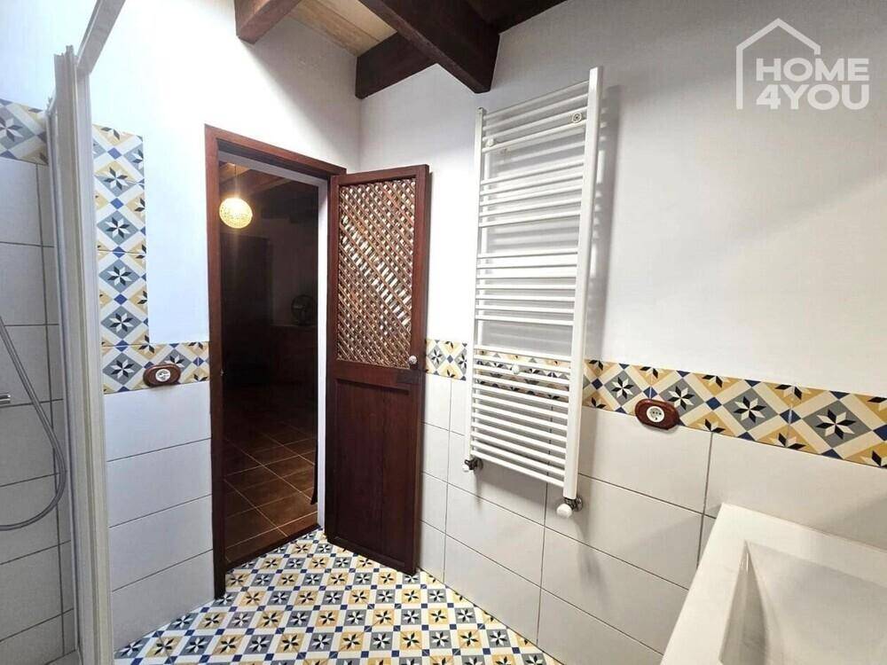 Badezimmer mit gemusterten Fliesen, Duschkabine und beheiztem Handtuchhalter unter Holzbalkendecke.