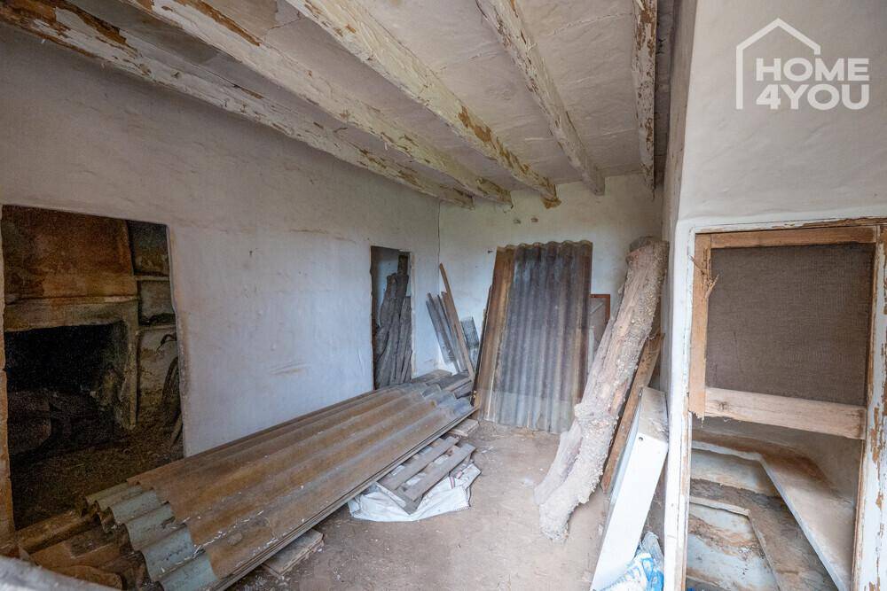 Innenraum mit verputzten Wänden, Holzbalkendecke und gelagerten Baumaterialien, stark renovierungsbedürftig.