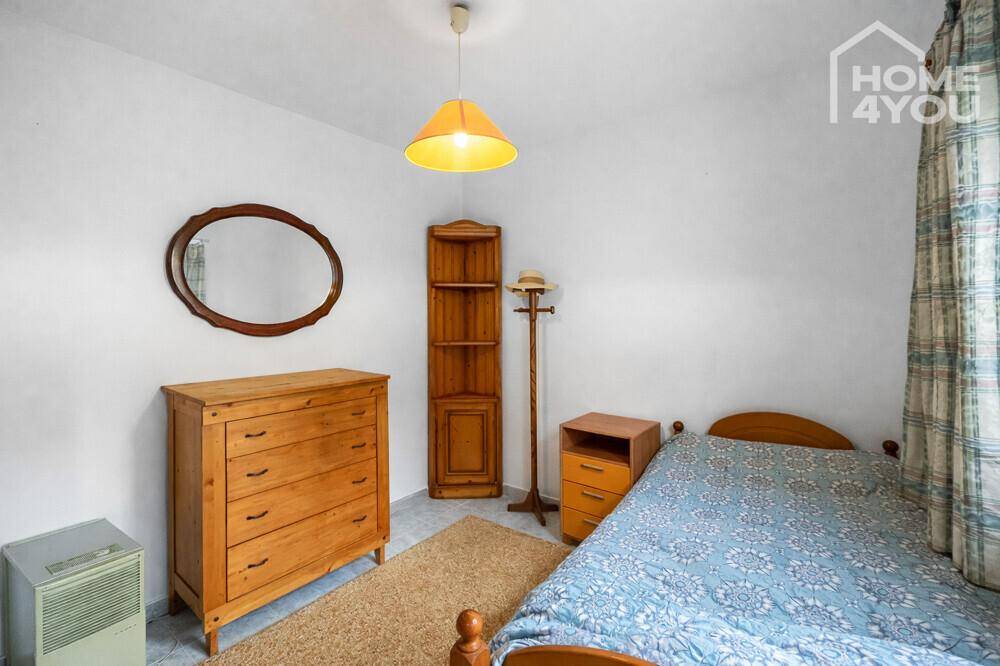 Einfaches Schlafzimmer mit Einzelbett, Kommode und einem kleinen Schrank.