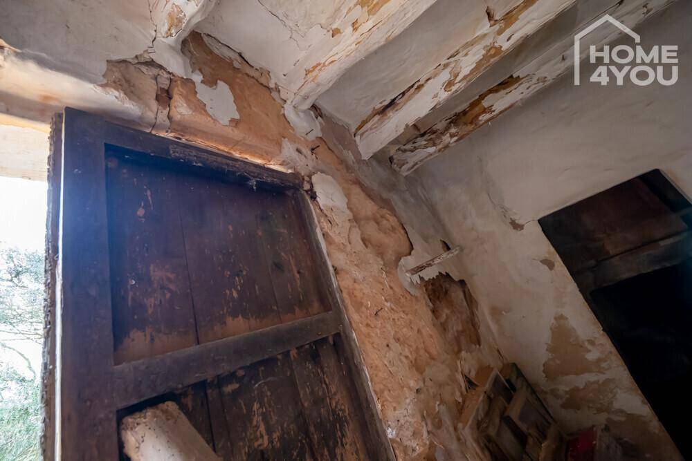 Alter Holztürrahmen mit stark beschädigten Wänden und Deckenbalken, deutliche Spuren des Verfalls.