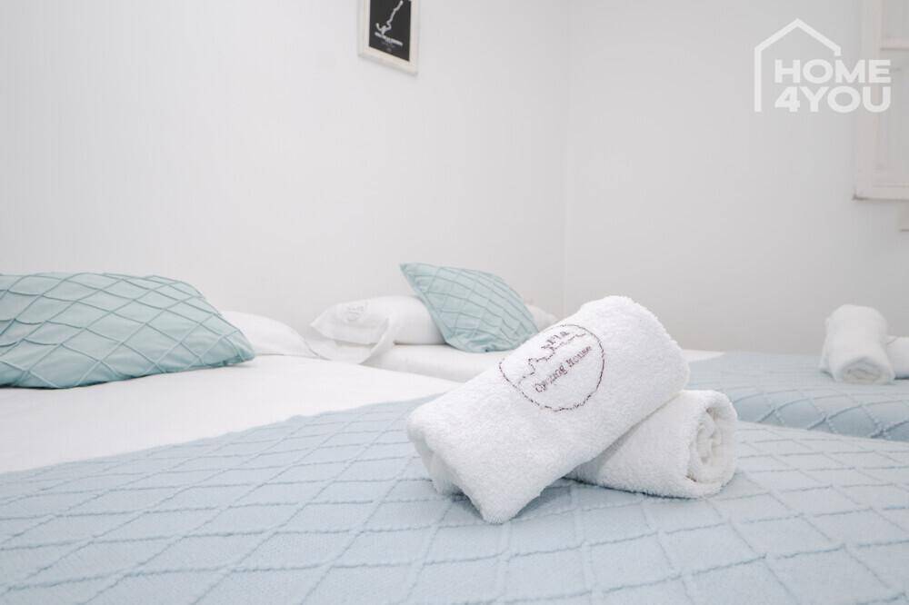 Nahaufnahme von Betten mit frischer weißer Bettwäsche und hellblauen Tagesdecken in einem Schlafzimmer.