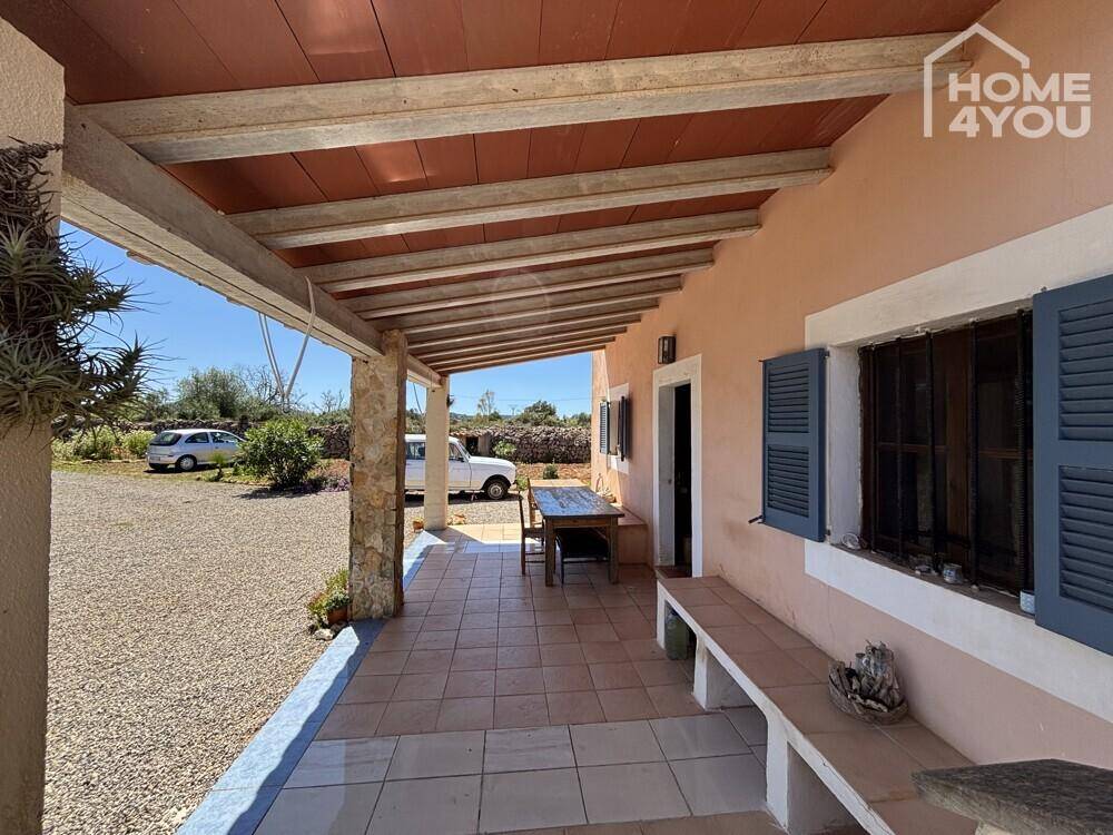 Überdachte Terrasse mit Fliesenboden, Holzbalken und einem Esstisch im Freien.