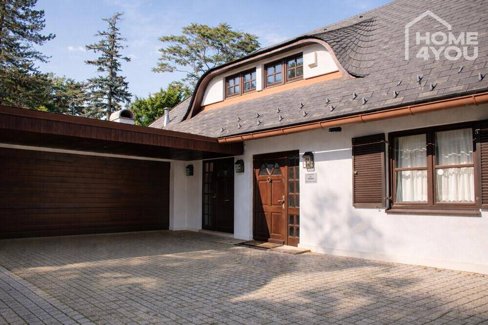 Eingangsbereich des Hauses mit Carport und gepflasterter Fläche unter blauem Himmel.