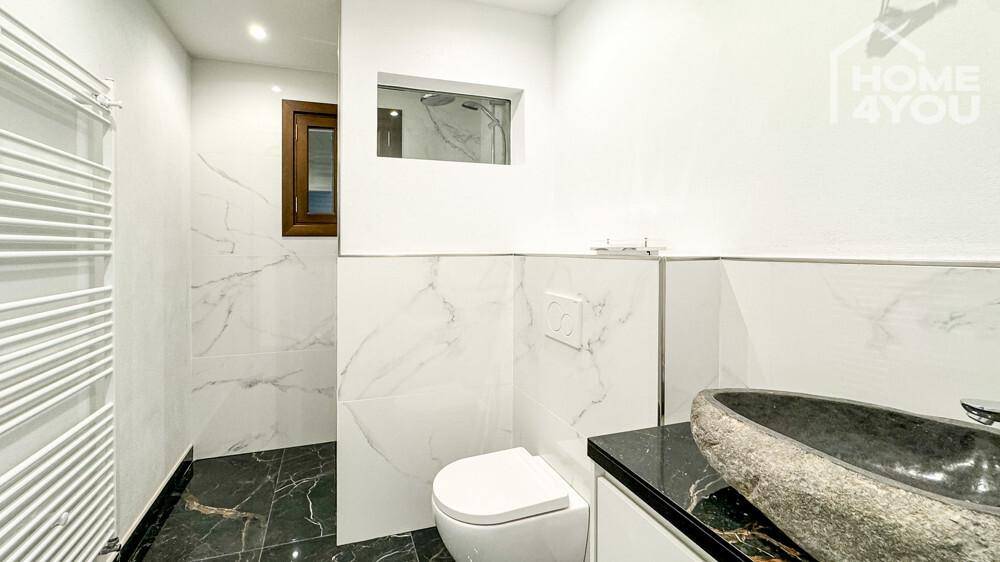 Elegantes Badezimmer mit Marmorfliesen, wandhängendem WC und beheiztem Handtuchhalter.