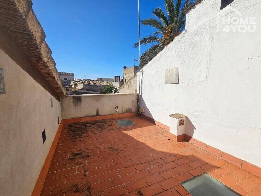 Dachterrasse mit Terrakottafliesen, niedrigen Mauern und Blick über die Dächer und Palmen.