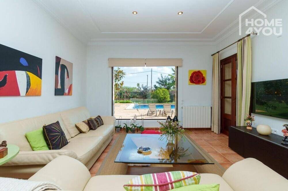 Helles Wohnzimmer mit beigen Sofas, Terrakottaboden und großem Fenster mit Poolblick.