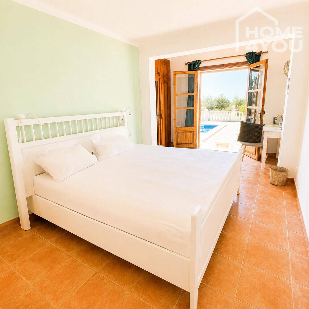 Helles Schlafzimmer mit weißem Bett und direktem Zugang zum Poolbereich im Freien.