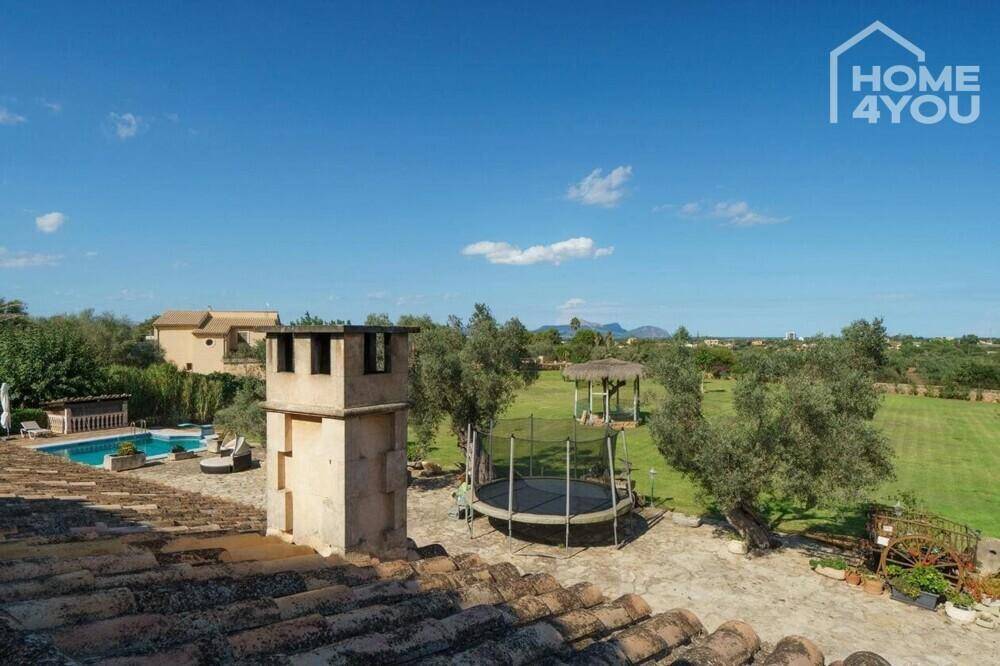 Blick über das Anwesen mit Pool, Trampolin und weitläufiger Grünfläche unter blauem Himmel.