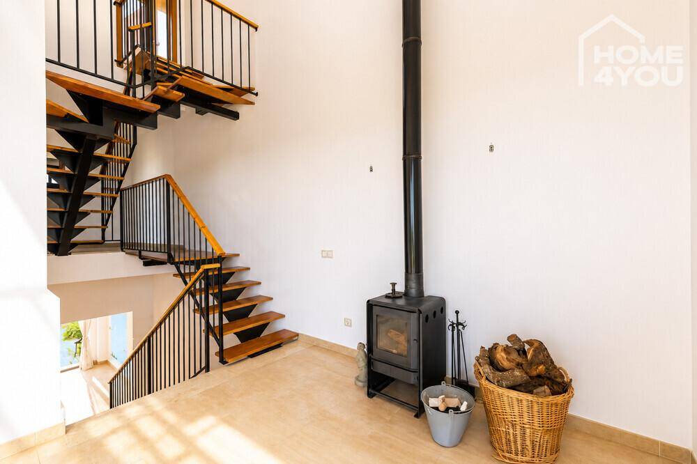 Geräumiger Wohnbereich mit Kaminofen, hohen Decken und offener Holztreppe.