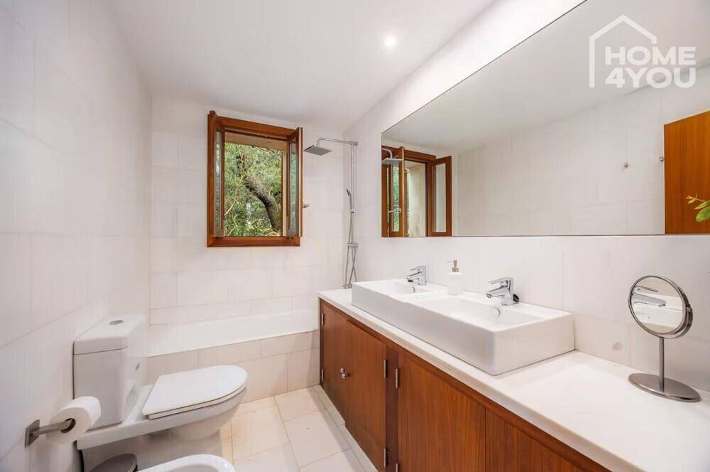 Modernes Badezimmer mit Doppelwaschbecken, großer Spiegelfläche und Fenster mit Blick ins Grüne.