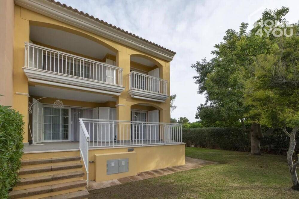 Gepflegter Gartenbereich mit Rasenfläche und Terrasse vor einem gelben Gebäude.