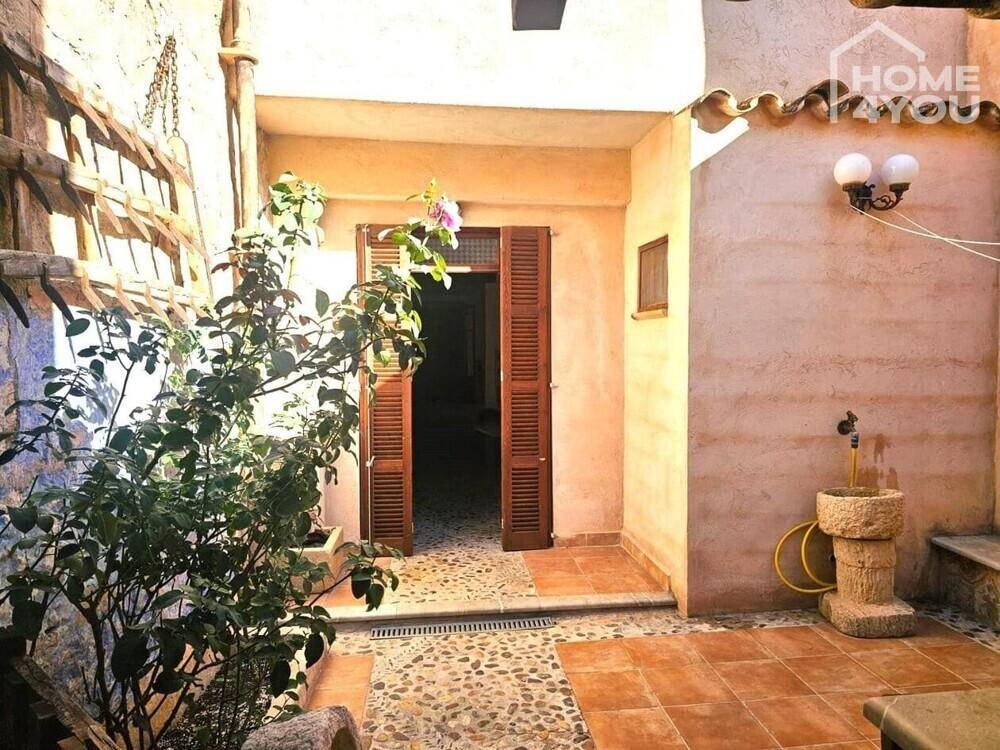 Mediterraner Innenhof mit Fliesen- und Kiesboden, Pflanzen und einem dekorativen Steinbrunnen.