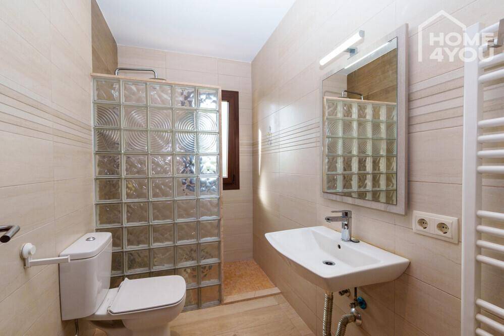 Modernes Badezimmer mit Duschbereich, WC und Waschbecken, abgetrennt durch Glasbausteine.