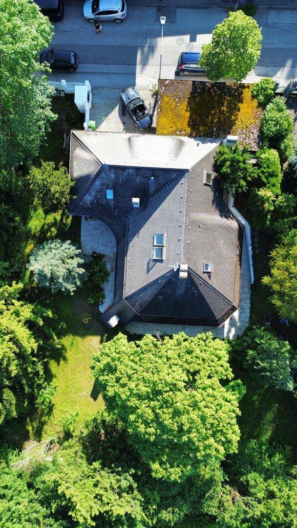 Luftaufnahme eines Hauses mit Satteldach, umgeben von Bäumen und einer Straße.