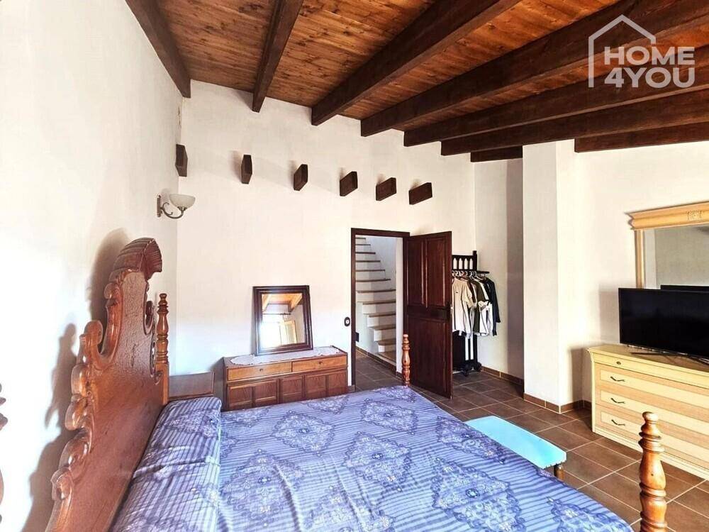 Schlafzimmer mit traditionellem Holzbett, Kommode und rustikaler Holzbalkendecke.