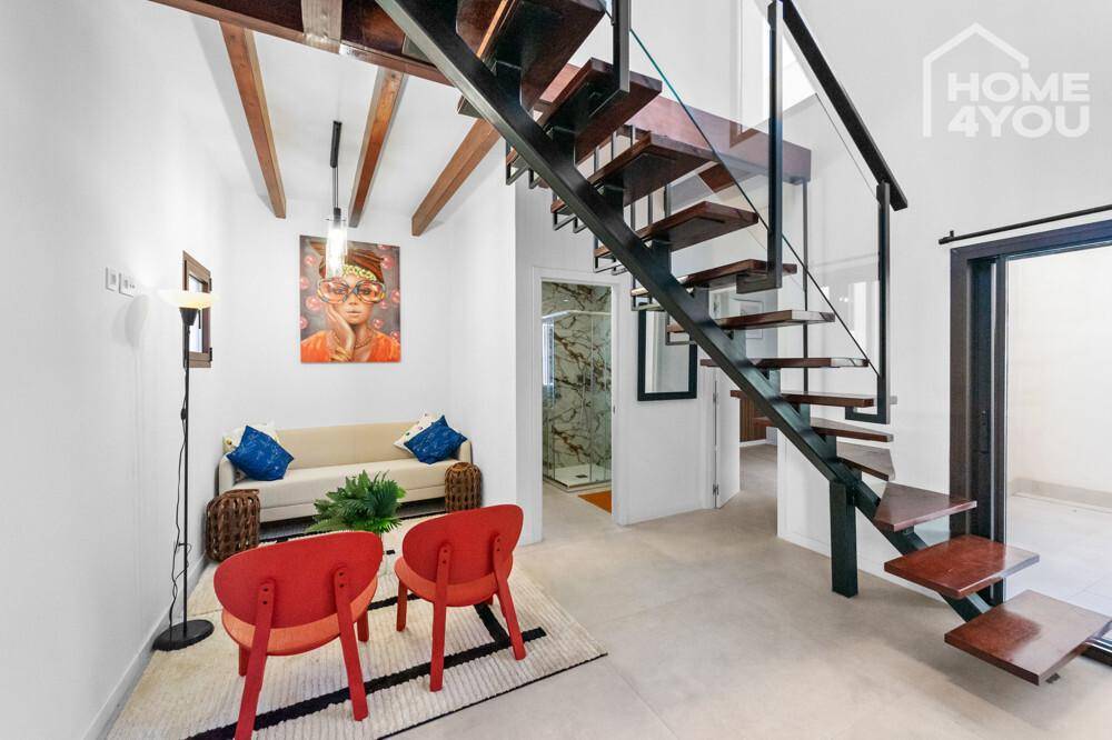 Helles Wohnzimmer mit moderner Treppe, bequemen Sitzgelegenheiten und charakteristischer Holzbalkendecke.