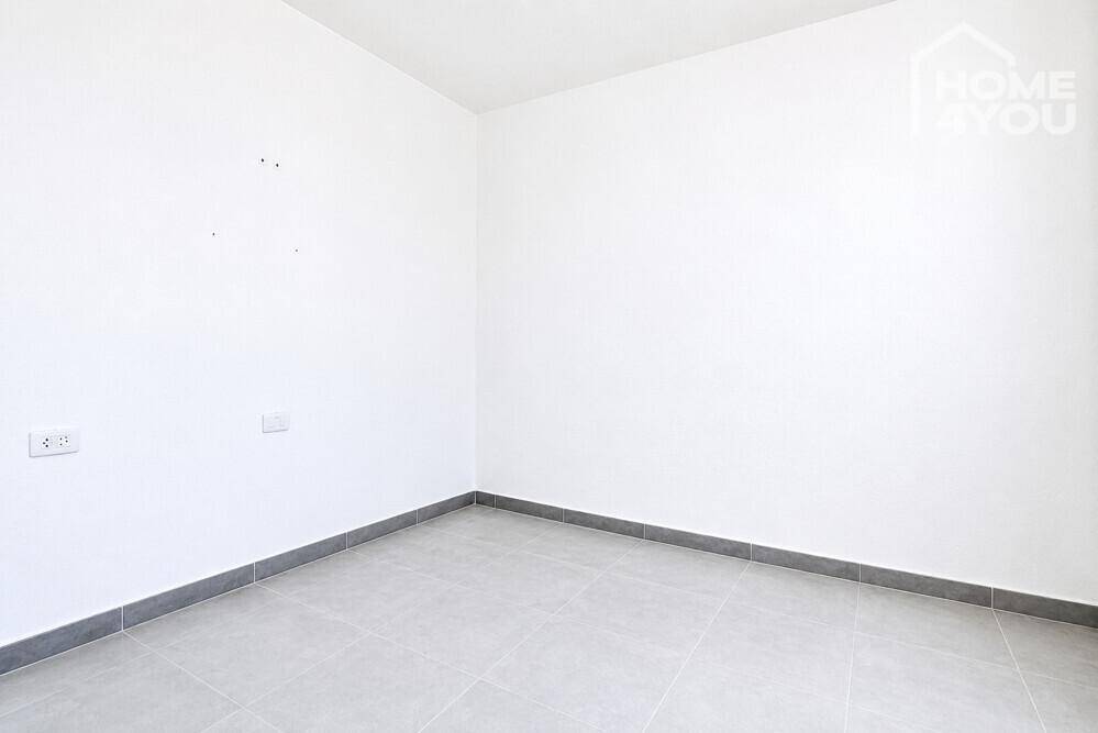 Leeres Schlafzimmer mit hellen Fliesen, weißen Wänden und grauen Fußleisten.