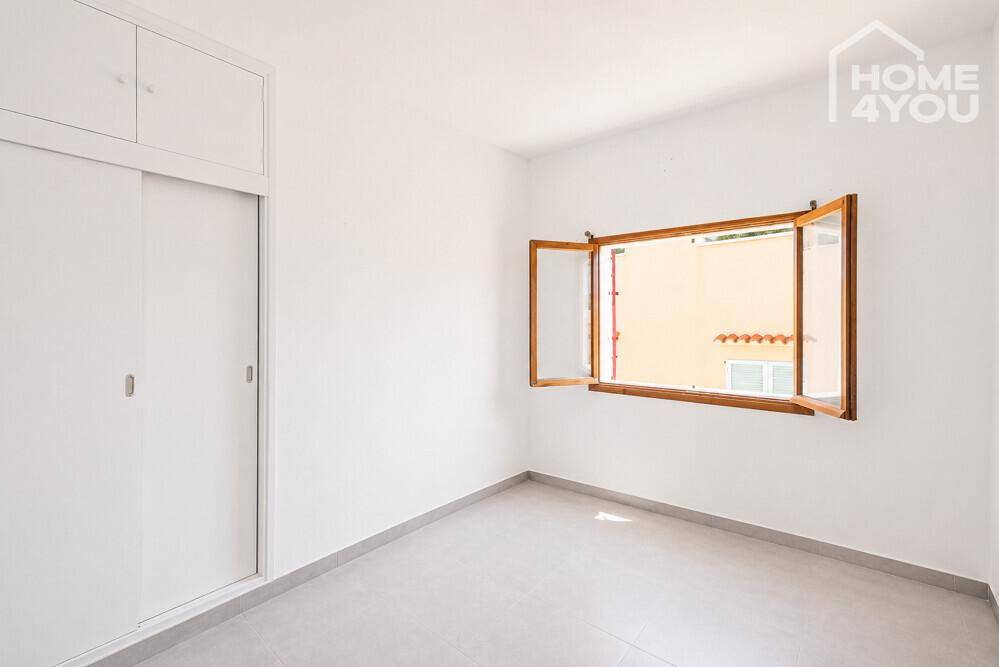 Schlafzimmer mit integriertem Schrank, Fliesenboden und einem Fenster mit Blick auf die Umgebung.