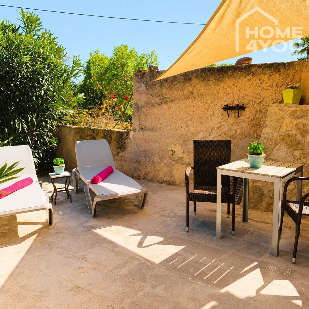 Sonniger Terrassenbereich mit Liegestühlen, Esstisch und Sonnensegel, umgeben von mediterraner Vegetation.