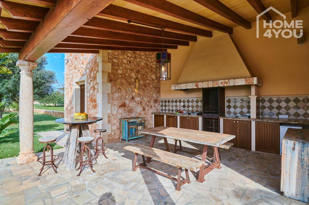 Detailansicht der Außenküche mit Grill, Holztisch und rustikalen Barhockern.