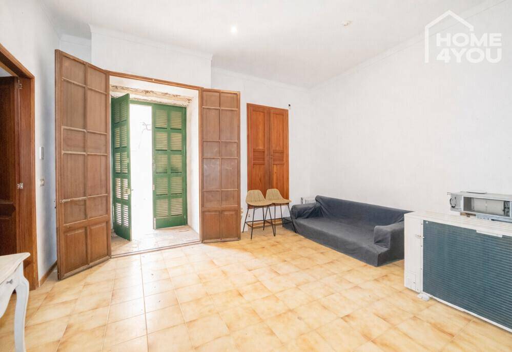 Wohnbereich mit Fliesenboden, Sofa und großen Holztüren, die nach außen führen.