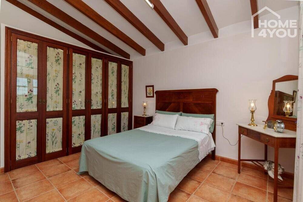 Schlafzimmer mit Doppelbett, Holzbalkendecke, Terrakottaboden und Einbauschränken.