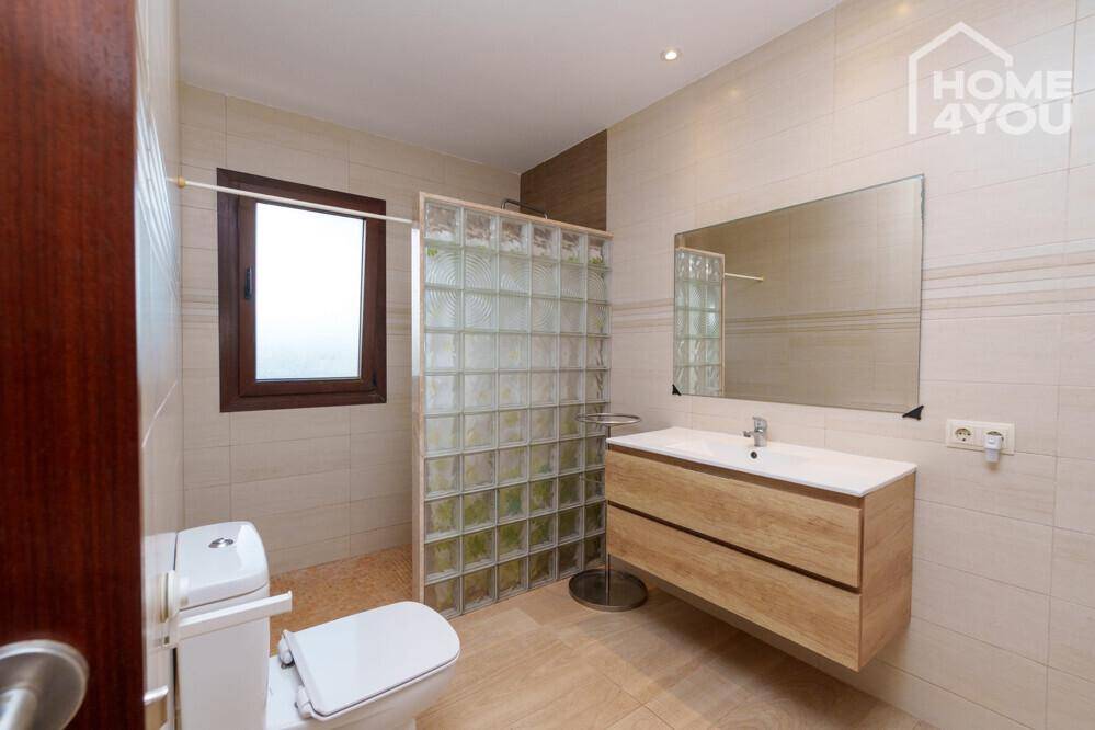 Zeitgemäßes Badezimmer mit schwebendem Holzwaschtisch, WC und Duschbereich mit Glasbausteinen.