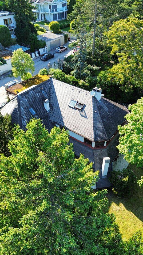 Detaillierte Luftaufnahme des Hauses mit Dachfenstern und umliegender grüner Landschaft.