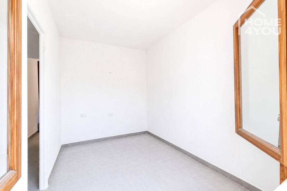 Schlichtes Schlafzimmer mit Fliesenboden, weißen Wänden und einem hohen Spiegel an der Wand.